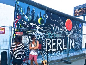 Man Wearing Black Waistcoat and White Tank Tops Standing Near a Mural  By Tomer Levi Forex